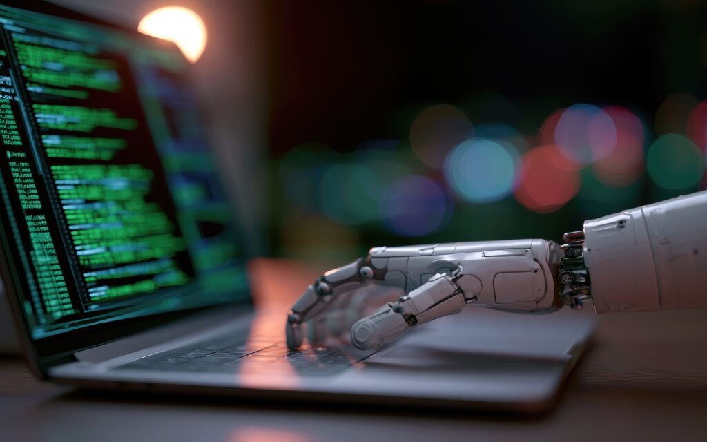A close-up shot of a robotic hand resting on a laptop keyboard, with lines of green code visible on the screen.